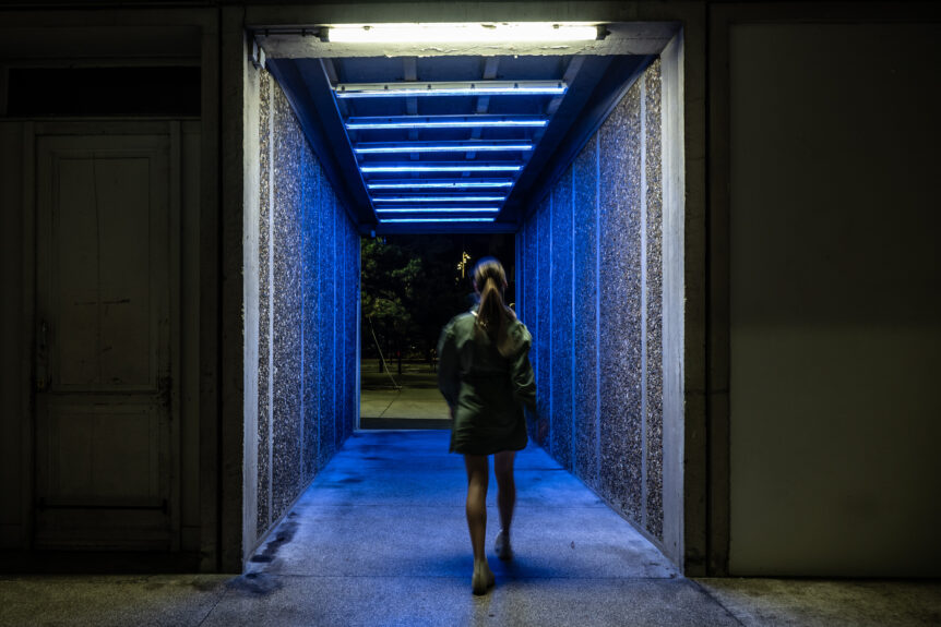 Une personne traverse un tunnel dans lequel sont installés des néons bleus.